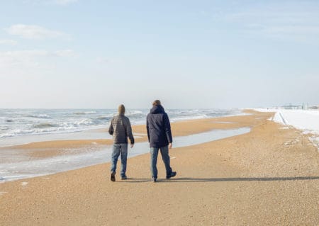Two men in warm jackets walking along the seashore