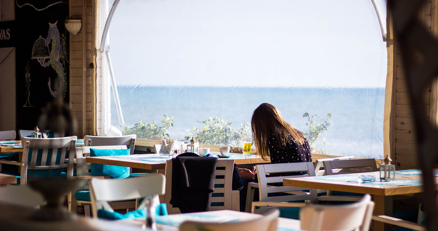 A woman in a restaurant sitting by the window enjoying the view of the beach
