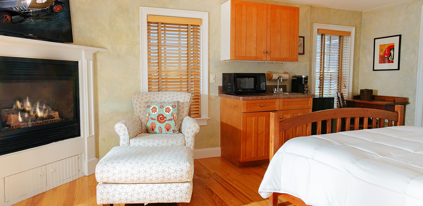Love seat by the fireplace at our hotel with glimpse of wet bar, workplace, and queen size bed at Mary Oliver room