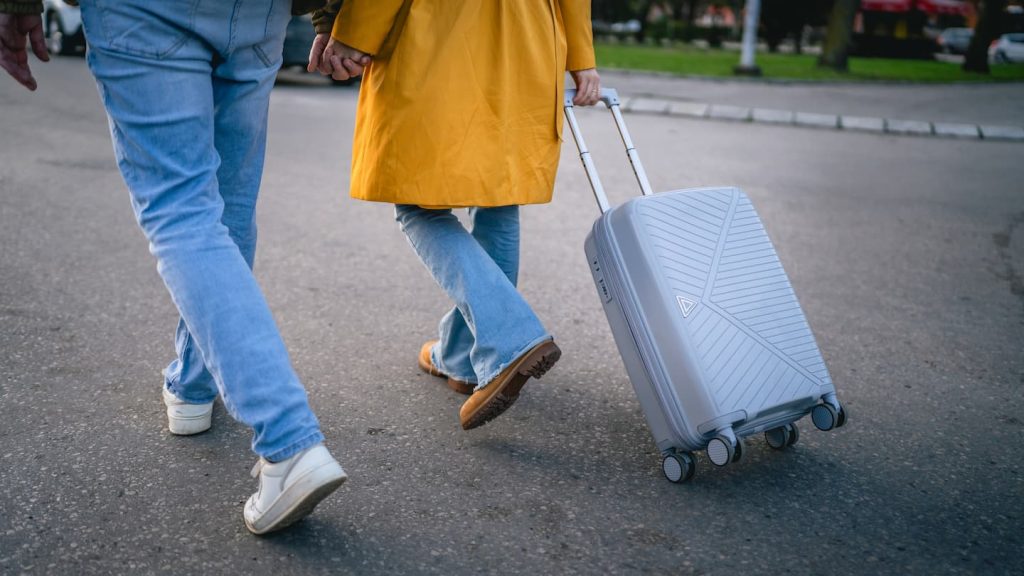 Back view of woman and man traveler dragging grey suitcase outdoor