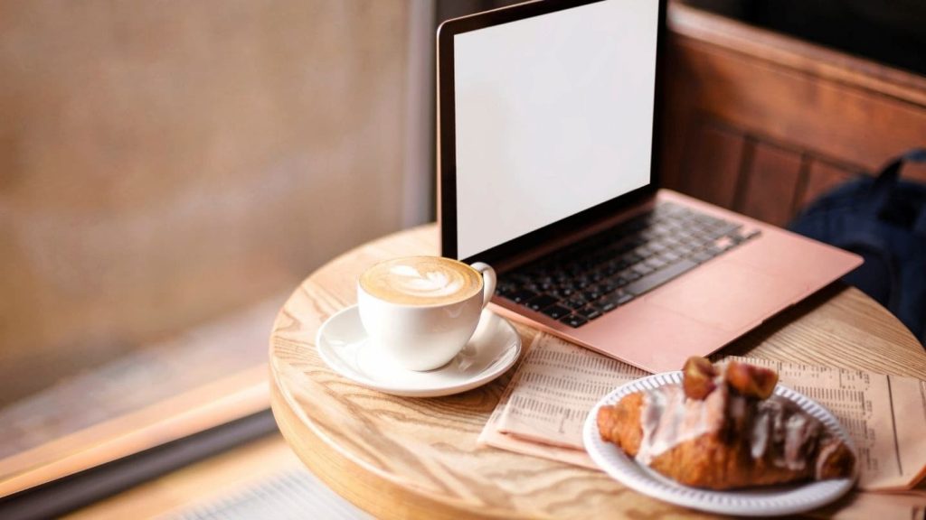 A laptop set on a table alongside a latte and croissant at a Provincetown coffee shop